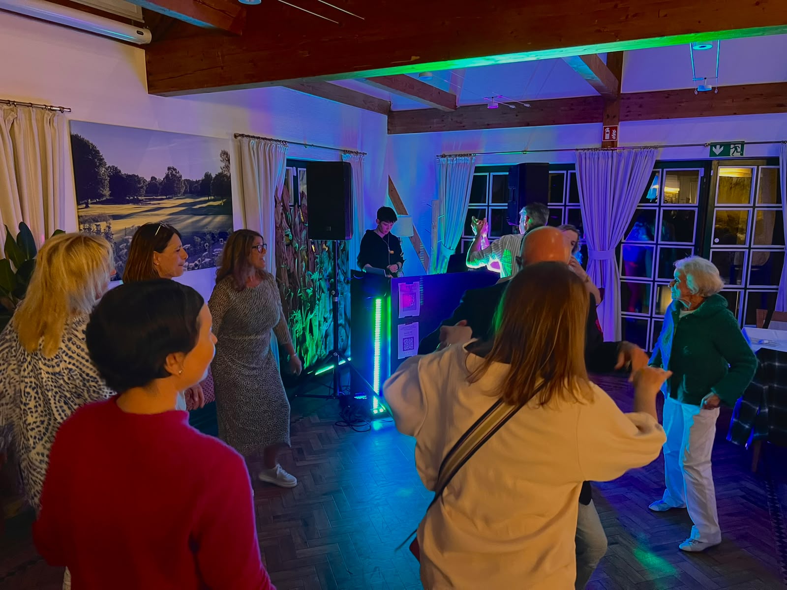 Feiernde Gäste tanzen bei einer Party mit DJ-Pult und grünem LED-Licht